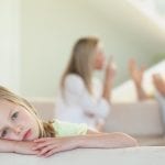 Sad young girl laying her head on a desk because of her parents arguing about divorce